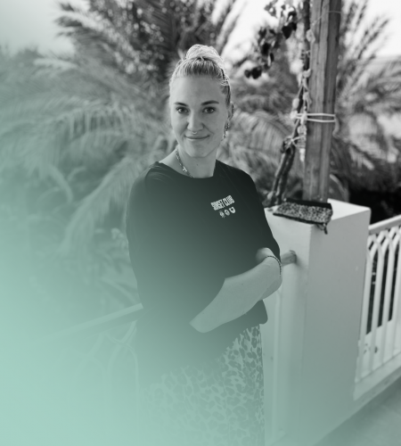 Porträtfoto von Stefanie Kaiser mit einem blonden Dutt und schwarzem T-Shirt vor Palmen. Sie blickt freundlich lächelnd in die Kamera. Unten im Bild stehen ihr Name "Stefanie Kaiser", ihre Position "Community Managerin" und ihre E-Mail-Adresse "hello@wearestudiox.de". Als Community Managerin in unserer Social Media Agentur übernimmt sie die Aktivität, wie Likes und Kommentare für die Kund:innen und beantwortet Nachrichten sowie Anfragen.